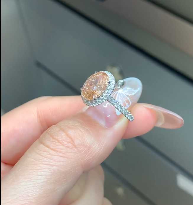 Peach lab diamond halo ring held between fingers showing clear lab diamond accents
