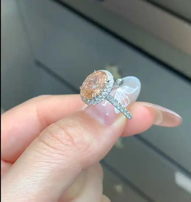Peach lab diamond halo ring held between fingers showing clear lab diamond accents
